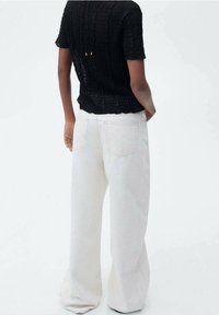 Blouse noire à texture avec manches courtes et pantalon blanc taille haute à jambes larges, doté de poches arrière et d'une coupe décontractée.
