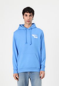 Lichtblauwe hoodie gemaakt van zachte stof, met een voorste kangaroo zak en een witte "Tommy Jeans" logo op de borst.