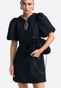 Fekete ruha puffos ujjal és kulcslyuk dekoltázzsal, fekete flitteres clutch táskával, ezüst lánccal.