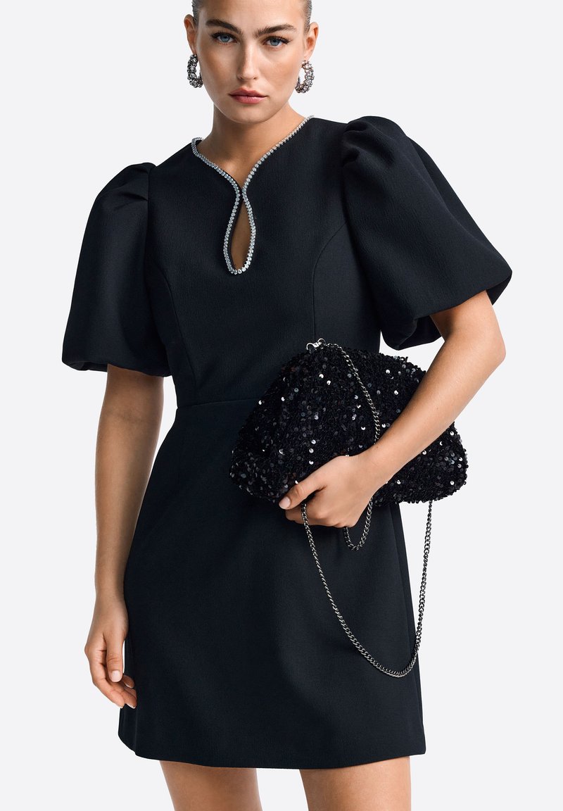 Fekete ruha puffos ujjal és kulcslyuk dekoltázzsal, fekete flitteres clutch táskával, ezüst lánccal.