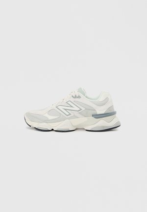 Weißer und grauer New Balance Sneaker mit Mesh- und Wildlederpaneelen, dicker Sohle und "N"-Logo an der Seite, auf einem schlichten Hintergrund präsentiert.