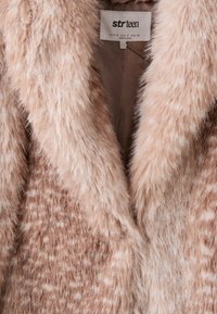 Gros plan d’un manteau en fausse fourrure beige et marron clair à motifs, avec un large col et une étiquette intérieure indiquant "strteen."