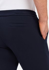 Marineblauwe sweatpants met een elastische tailleband, zijzakken en een achterzak voor opslag. Gemaakt van een zachte stof met een gladde textuur.