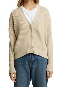Beige gebreide cardigan met een v-hals, knoopsluiting, ribbeltextuur en verlaagde schouders. Gepaard met blauwe jeans.