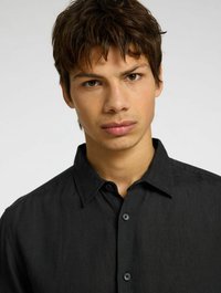 Camisa de lino negra con collar clásico, con cierre de botones y tejido texturizado. El diseño ajustado realza la visibilidad del escote.