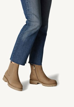Bottines en cuir marron à fermeture éclair sur le côté, avec des panneaux texturés et des semelles en caoutchouc, associées à un jean en denim bleu court.
