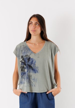 Top in cotone grigio a maniche corte e scollo a V, caratterizzato da una stampa floreale blu sul lato sinistro e un fit rilassato e cropped.