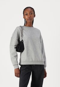 Gray sweatshirt with a crew neckline and dropped shoulders, paired with black wide-leg jeans and a small black shoulder bag with a silver chain strap.