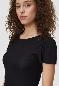 Schwarzes, geripptes Kurzarmoberteil mit Rundhalsausschnitt, präsentiert auf einer Person mit lockigem Haar, mit einem figurbetonten Schnitt und weichem Material.