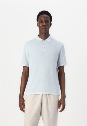 Polo bleu clair à manches courtes, avec patte de boutonnage à trois boutons, col côtelé, tissu texturé, associé à un pantalon beige clair.
