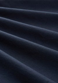 Tmavě modrý textil s hladkým povrchem, vykazující jemné rýhy a záhyby, což naznačuje lehký a flexibilní materiál.