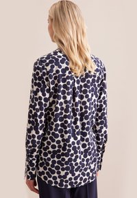 Camicia a maniche lunghe con un motivo circolare blu navy e bianco, tessuto liscio, colletto classico e polsini abbottonati. Retro con orlo rotondo.