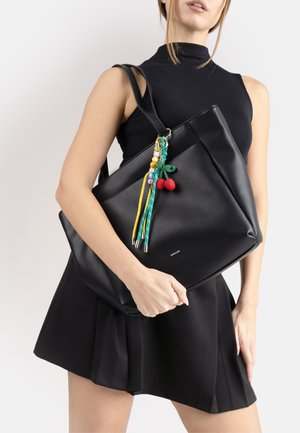 Donna con vestito nero senza maniche che tiene una grande borsa tote in pelle nera con portachiavi colorato di perline e tessuto a forma di ciliegia.