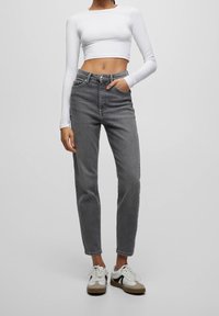 Jeans grigi alti in vita con design a gamba dritta e cinque tasche, abbinati a un crop top bianco a maniche lunghe e sneaker bianche.