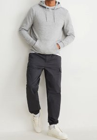 Grå huvtröja med känguruficka, i kombination med svarta cargo-byxor med sidofickor, och vita sneakers med snörning.