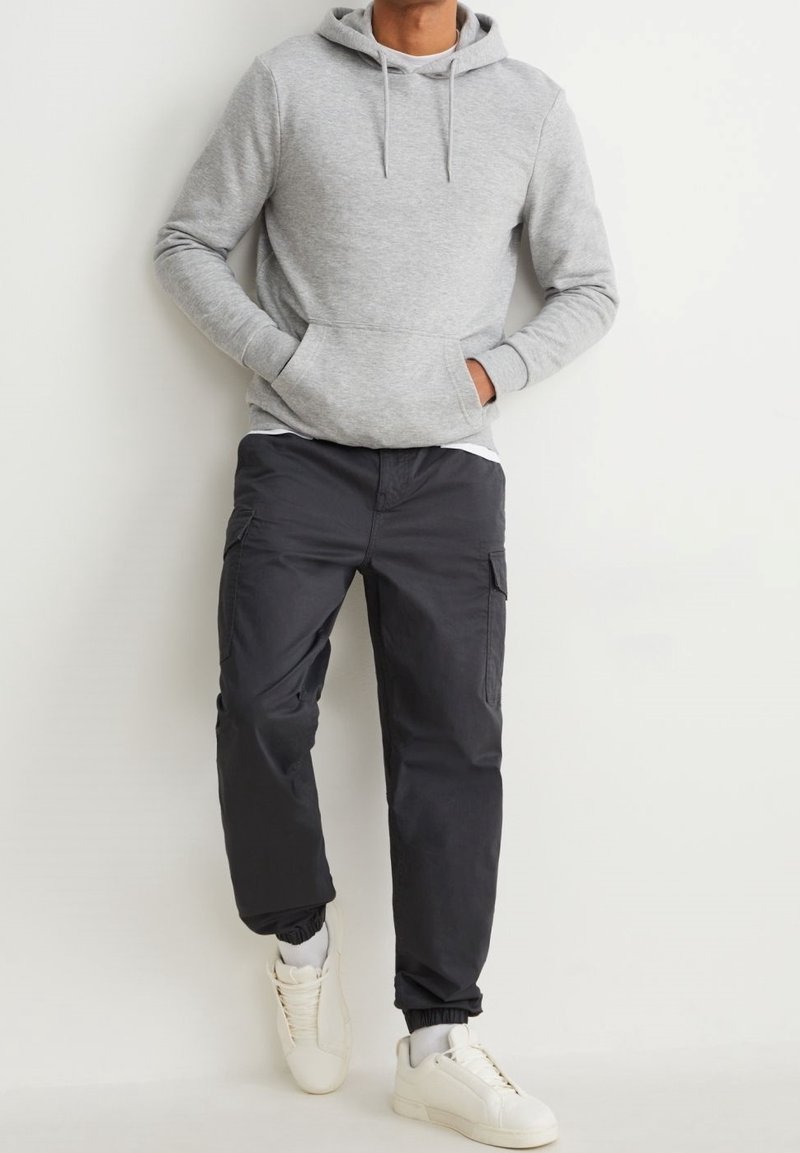 Grå huvtröja med känguruficka, i kombination med svarta cargo-byxor med sidofickor, och vita sneakers med snörning.