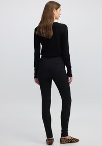 Czarne dopasowane legginsy o gładkiej teksturze i minimalnych szwach. Połączone z czarną bluzką z długim rękawem oraz balerinami w zwierzęcy wzór z ostrymi noskami.