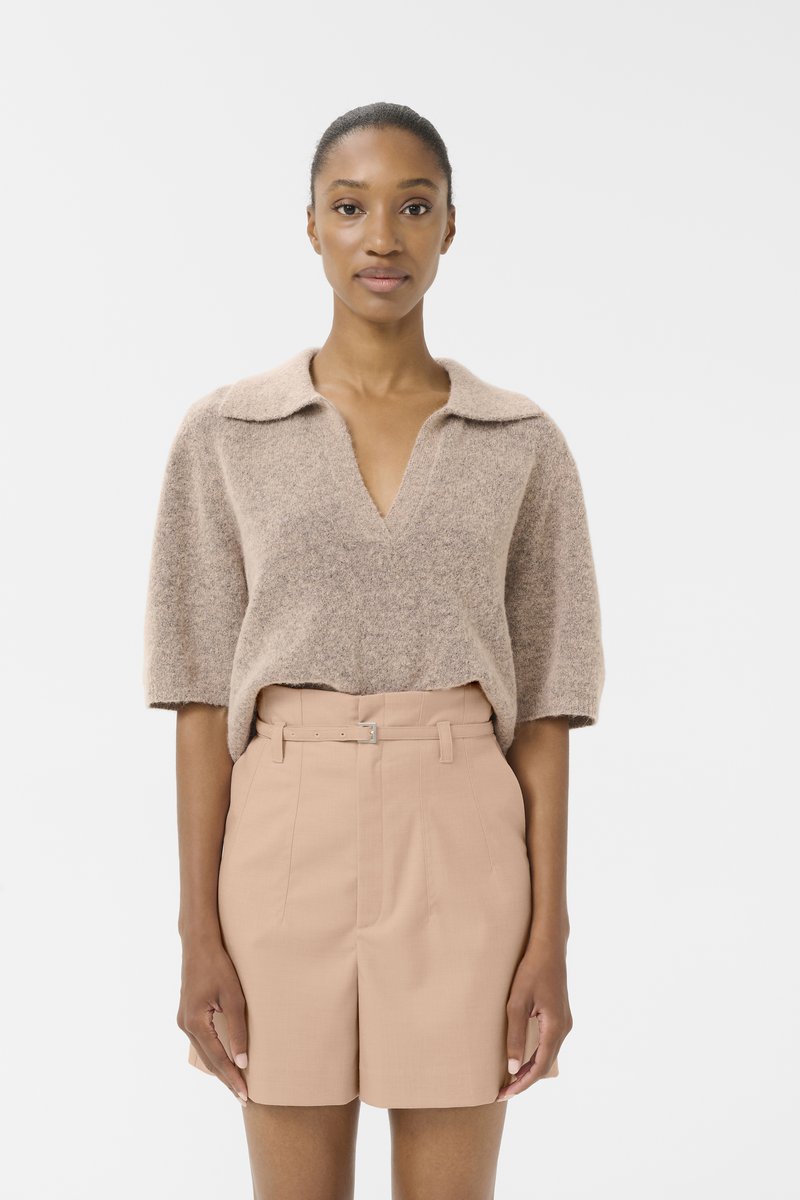 Kort, beige, teksturert strikket genser med V-hals og korte ermer, sammen med lyse rosa skreddersydde shorts med belte i livet.