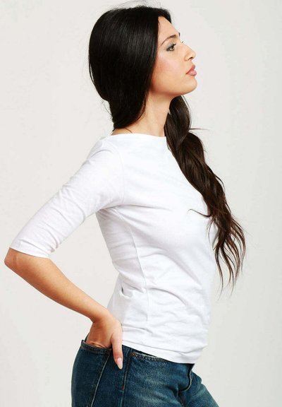 Maglietta bianca a maniche 3/4 in cotone, con scollatura rotonda e silhouette aderente, indossata con jeans in denim blu.