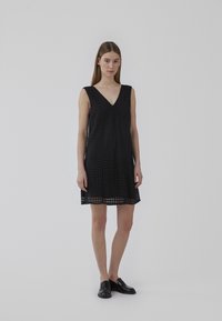 Robe noire sans manches avec décolleté en V, présentant un motif en grille texturé et une coupe ample, se terminant au-dessus du genou. Ourlet simple et style épuré.