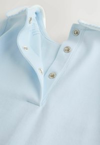 Lyseblå polo-shirt med krave og sølvfarvede trykknapper samt kontrasterende hvid kant langs kraven og åbningerne.