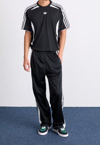 Musta urheiluasu, jossa on lyhythihainen pelipaita valkoisilla koristeilla ja siihen sopivat housut sivuviivoilla. Yhdistetty mustiin ja vihreisiin lenkkareihin.