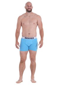 Boxers bleus en matériau élastique, avec une ceinture blanche portant le logo "RUCKFIELD". Texture lisse, design ajusté.