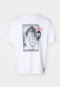 Bílé bavlněné tričko s krátkými rukávy, které obsahuje černobílý grafický design lví tváře a siluetu osoby.