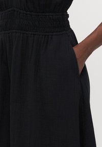 Black dress featuring a textured fabric, elastic waistband, and side pockets, with a smooth, flowing design visible in the lower section.