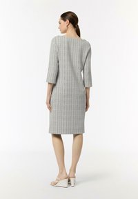 Abito grigio, con texture, maniche a tre quarti e taglio dritto. Presenta una scollatura sulla schiena ed è abbinato a sandali con zeppa bianchi.