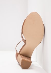Sandale à talon carré marron pour femmes vue du côté de la semelle sur fond d'angle blanc.