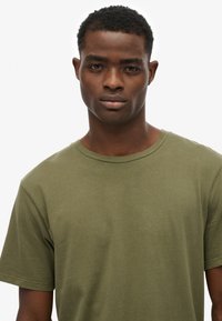 Oliwkowa bawełniana koszulka z okrągłym dekoltem, krótkimi rękawami i miękką fakturą. Prosty, nieozdobiony wzór bez widocznych nadruków.