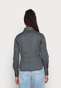 Gray, fitted jacket made from a lightweight material with a crisp collar and buttoned cuffs, featuring a back seam and subtle logo detail.