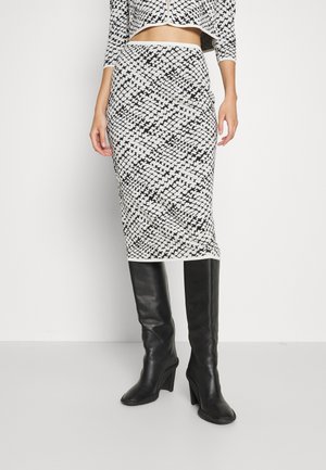 Strick-Bleistiftrock mit einem schwarz-weißen geometrischen Muster, kombiniert mit knielangen schwarzen Lederstiefeln und einer passenden kurz geschnittenen Jacke.