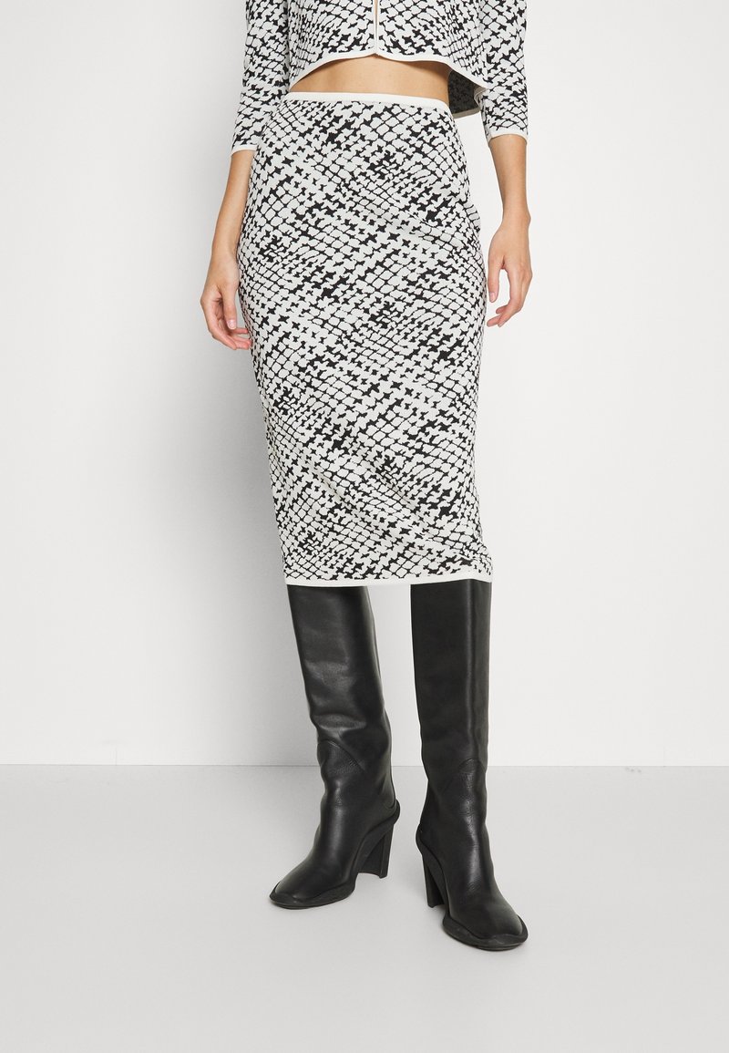 Stickad pennkjol med ett svart och vitt geometriskt mönster, matchad med knähöga svarta läderstövlar och en matchande kort jacka.