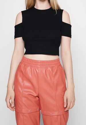 Mujer con top corto negro de hombros descubiertos y pantalones de cuero sintético coral de cintura alta con detalles de botones de presión.