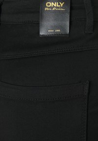 Jeans en denim noir avec une poche arrière, une étiquette en cuir avec du texte doré et des coutures contrastantes le long des coutures.