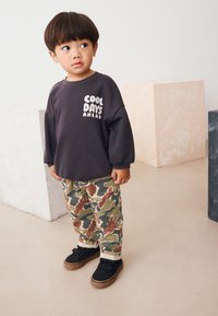 Sweat-shirt gris foncé avec le texte "COOL DAYS AHEAD", assorti à un pantalon cargo camouflage vert, marron et beige, et des baskets noires à scratchs.