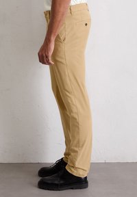Jasno. beżowe spodnie o prostym kroju, wykonane z gładkiego materiału. Posiadają kieszenie boczne oraz jedną tylną kieszeń z zapięciem na guzik.