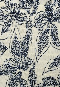 Weißer Stoff mit einem marineblauen Blumenmuster, ausgestattet mit geraffter Textur und wechselnden Streifen. Das Design zeigt filigrane Blattmuster.