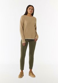 Beige gerippter Strickpullover mit langen Ärmeln, kombiniert mit olivgrünen Slim-Fit-Hosen und beigen Sneakers. Einfaches Design mit kontrastierendem Ausschnitt.
