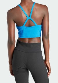 Blå atletisk crop top med ett korsat ryggdesign, kombinerad med högmidjade svarta leggings som visar en slät tygtextur.