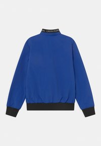 Niebieska bomberka z wysokim kołnierzem, czarnymi prążkowanymi mankietami i dołem oraz z markowym dekoltem. Charakteryzuje się gładką, lekką fakturą.