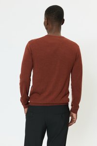 Hosszú ujjú, rozsdabarna pulóver kerek nyakkal, texturált anyagból készült. Feketére szabott nadrággal párosítva, amelyen két hátsó zseb található.