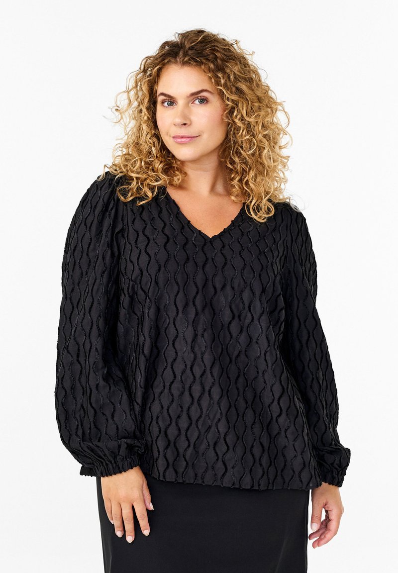 Blusa nera realizzata in tessuto testurizzato con motivi ondulati, scollo a V, maniche a palloncino elastiche e vestibilità rilassata. Progettata per comfort e stile.