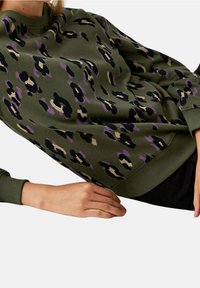 Sweatshirt vert olive avec un motif léopard en noir, beige et violet. Le design comprend des poignets et un col côtelés.