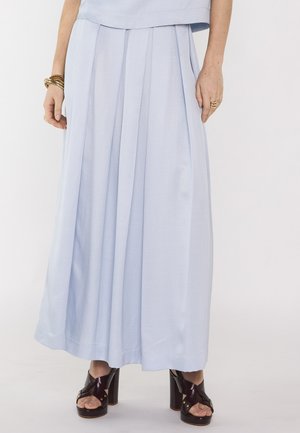 Pantalon large taille haute bleu clair associé à des talons compensés noirs à bouts ouverts, anneaux dorés aux doigts et bracelets au poignet gauche.