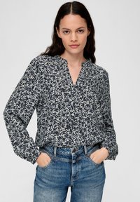 Navybluse mit weißem Blumenmuster, langen Ärmeln, V-Ausschnitt und lockerer Passform, kombiniert mit hellblauen Jeans.