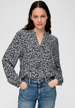 Navybluse mit weißem Blumenmuster, langen Ärmeln, V-Ausschnitt und lockerer Passform, kombiniert mit hellblauen Jeans.