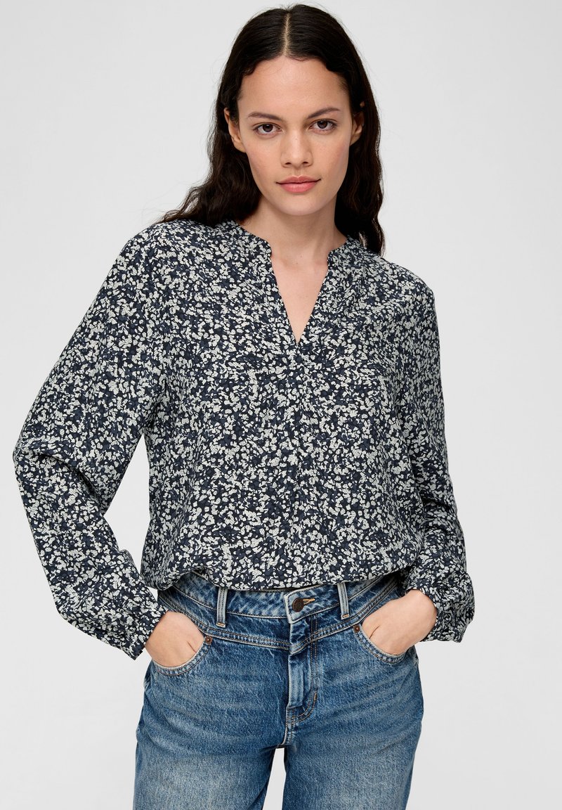 Navybluse mit weißem Blumenmuster, langen Ärmeln, V-Ausschnitt und lockerer Passform, kombiniert mit hellblauen Jeans.
